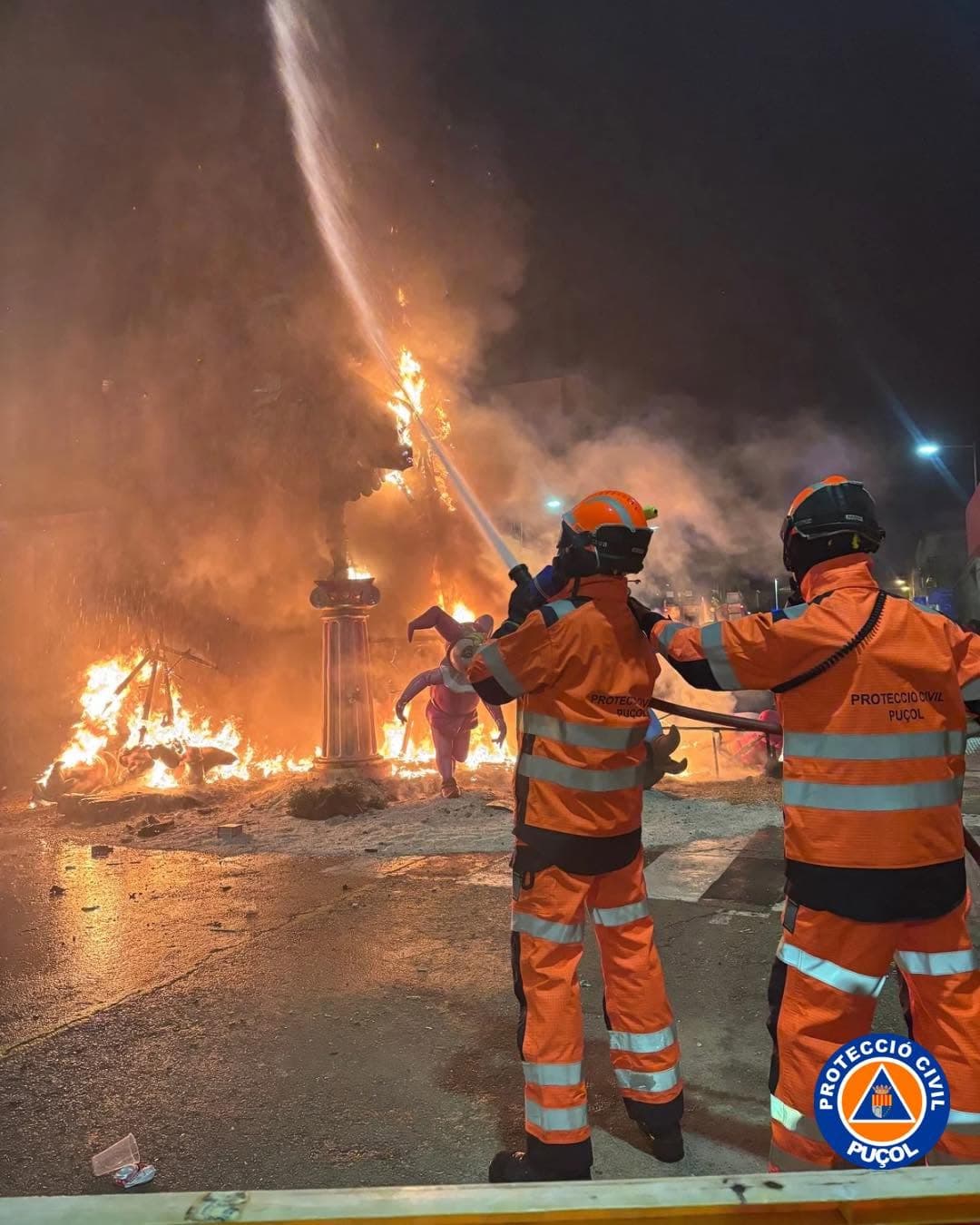 Personal de Protecció Civil Puçol con equipo de protección y una manguera durante una intervención nocturna con fuego.